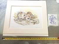 Framed lithograph matted but unframed resting on a surface with measuring tape showing size