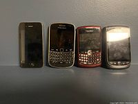 Photo of all four phones showing front faces: one iPhone 4 and three BlackBerry models with QWERTY keyboards and touchscreen.