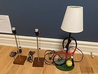 Photo of two matching metal and wood lamp stands without lampshades and one tennis themed lamp with tennis rackets and ball on green base