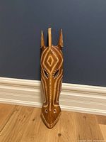 Front view of elongated wooden decorative mask with pointed ears and white dot patterns
