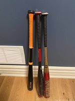 Three baseball bats standing upright against a blue wall, showing color and grip details