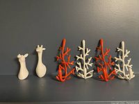 Six clothing hangers arranged against a dark background, featuring two white giraffe-shaped hangers, two red branch-style hangers, and two white branch-style hangers.