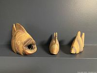 Three wooden fish figurines arranged in a line showing front and side views against a dark background.