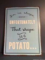 Front view of the rectangular metal sheet showing the humorous quote with decorative font and light blue background.