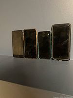 Four iPhones standing upright side-by-side showing screens and cases, all used and non-working.