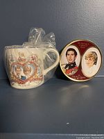 Photo showing mug and sweets tin side by side on a blue surface against a blue background. Mug is wrapped in clear plastic.