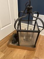 Side view of smoked glass hanging light with black metal frame and four bulbs inside, resting on cardboard.