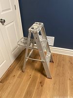 Full side view of an aluminum step ladder showing paint splatters and three steps plus top platform.