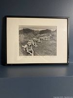 Framed black and white photograph showing a row of yellow Labrador dogs lying outdoors.