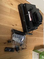 Sony Hi-Fi Stereo VCR and Bell device stacked with remotes and cords on wooden floor.