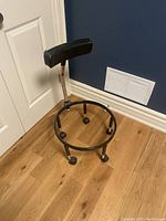 Metal yoga ball chair frame with padded backrest, missing yoga ball, shown against wooden floor and blue wall.
