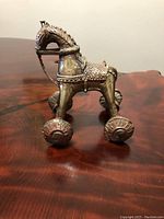 Front left angle of the antique bronze horse pull toy on wheels displaying detailed embossed patterns and patinated bronze finish.
