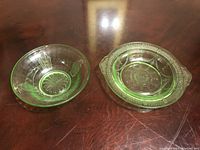 Two green uranium glass bowls with visible rim blemishes on a wooden surface.