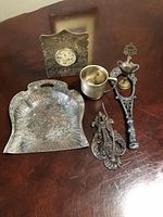 Photo showing brass and jade insert bookend with clock face, ornate metal dustpan, two metal finials including a receipt spike, and a small metal cup.