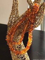 Close-up of the amber bead necklace draped over part of a display stand, showing the warm tones and bead shapes.