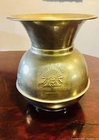 Full front view of vintage brass spittoon on wood surface with embossed logo visible.