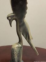 Side view close-up of intricately carved bird with downturned beak on cylindrical pedestal