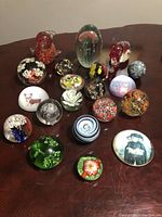 Full view of all 20 items showing various glass paperweights and the jade sphere on a wood table