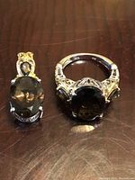 Pair of 925 sterling silver filigree jewelry items: a ring and pendant, both with oval topaz colored stones in prong settings, shown on a wooden surface.