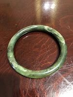 Top view of the jade bangle showing circular shape and natural color variations in green tones with some darker veins and mottling.