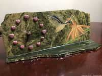 Full view of the jade mantel clock showing the green jade with hand-painted hummingbird dipping into orange hibiscus flowers. Pink rhodium hearts mark hours on clock face.