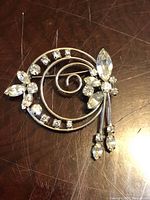 Front view of Jay Flex sterling silver brooch with circular floral spray design and clear rhinestone crystals on a wooden surface.