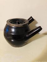 Side angle view showing rounded dark glazed stoneware teapot with side handle and angled spout.