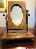 Front view of the wooden dresser valet mirror showing oval mirror and base with recessed trays.