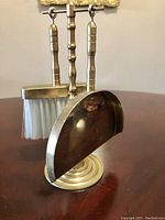Front view of the vintage brass butler's brush and pan set on the stand showing the brush and dustpan hanging.