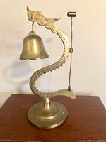 Front view of vintage brass dragon bell with hanging bell and striker rod.