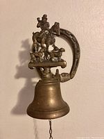 Frontal close-up view of the vintage brass shopkeepers bell showing horse rider figurine, dogs, and bell body with pull chain.