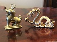 Front view of the two brass figurines showing the dragon and foo dog on a wooden surface.