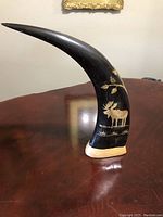 Side view of the carved horn with moose and leaf design showing the detailed artwork on the surface.