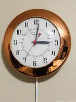 Front view of the round copper frame clock with clear clock face and hands visible.