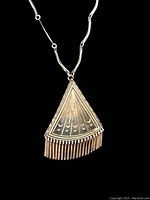 Front view of vintage fan-shaped sterling silver pendant with detailed engravings and fringe on black background.