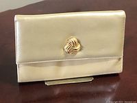 Front view of vintage tan beige leather clutch purse with a gold-tone twisted knot embellishment on the front flap.