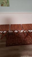 Three eucalyptus wood fold-up tables placed side by side, showing square slatted tops and folding X-leg design.