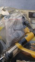 Photo of the handheld sandblaster gun with yellow handle and chrome nozzle inside original packaging, partially obscured by plastic packaging.