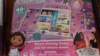 Front of the game box showing the Gabby's Dollhouse Meow-mazing Game board layout with character illustrations and game mechanics.