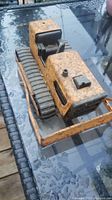 Full view of the bulldozer showing rusted yellow metal body, rubber tracks, black seat, and front blade detail.