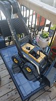 Photo of vintage Tonka Strong Arm toy loader parked on a table with nearby plants in the background, showing the loader arm, wheels, and cab.