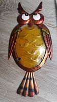 Metal and glass owl wall art showing rust-colored metal with yellow glass body and large white eyes.