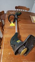 Full view of Yardworks electric weed whipper strimmer placed on wooden table, showing long shaft, handle and cutting head with guard.