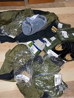 Items including unopened green Canadian military crew neck pullovers, black dress shoes, socks, and Russian military toque on floor.