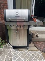 Full view of Char-Broil stainless steel gas barbecue grill with cabinet doors, control knobs, and temperature gauge on the hood. Located outdoors on a patio.