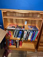 Front view of pine wood bookcase filled with books and comics, showing four fixed shelves and overall wear on wood surfaces.