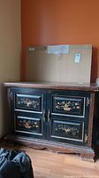 Front view of wood credenza showing two painted doors with tree and potted plant design, metal knobs, dark wood finish, scratches on top and base visible.