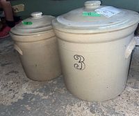 Pair of stoneware crocks with lids, sizes 3 and 9, sitting on concrete floor.