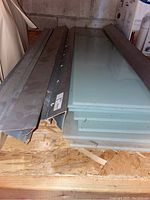 Stack of eight frosted glass shelves with metal hanging brackets on left, placed on wooden surface.