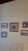 Five assorted framed prints hanging on the wall featuring moons, horses, embroidered flowers, and scenic views.